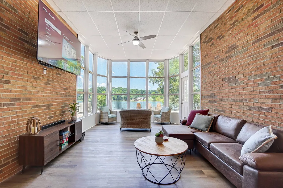 A comfortable seating area faces large windows that frame captivating outdoor views. A TV is mounted on the wall, and the bright, open space is ideal for unwinding, socializing, or watching movies together as the sun sets beyond the river.