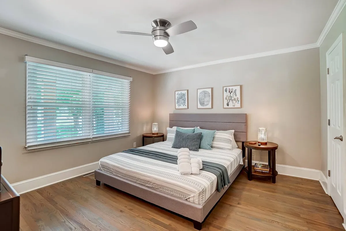 A serene bedroom centered on a comfortable bed with decorative pillows, tasteful artwork above the headboard, and matching nightstands. The soft lighting and minimalist decor create a peaceful space for relaxation and restful sleep.