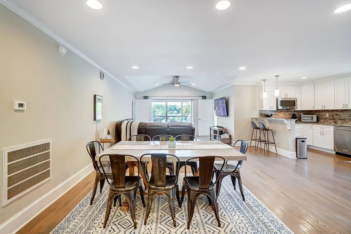 A warm and inviting dining space with a large table set within an open layout, offering a direct view of the adjacent kitchen area and large window. The scene is set for family meals or festive gatherings, filled with natural light and cheerful ambiance.