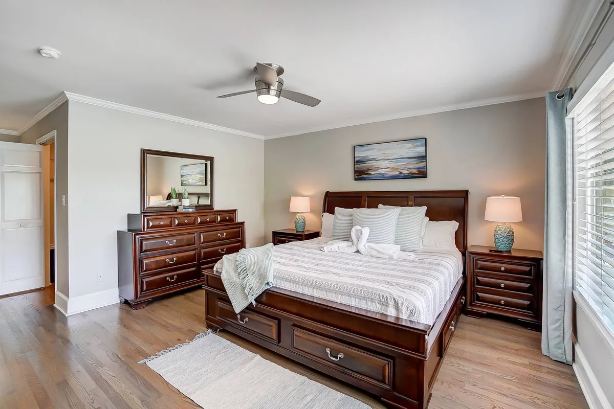 A tranquil bedroom featuring a king-size bed adorned with plush pillows and cozy bedding. Flanked by nightstands and a wooden dresser, the space exudes comfort and style, with natural light streaming from a nearby window, creating a calming retreat ideal for restful nights.