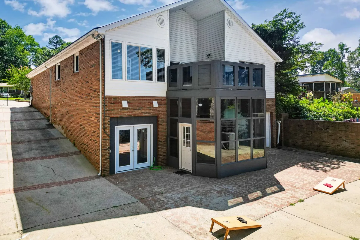 A view of a modern glass-enclosed room adjacent to a brick exterior, with an outdoor game setup on the lawn. The scene captures people gathering for outdoor games, social events, and relaxed recreation in a sunlit, casual setting.