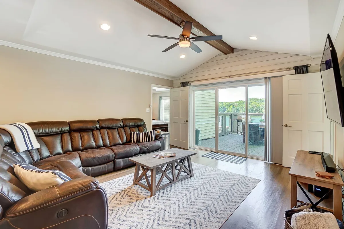This image presents a cozy leather sectional sofa and wooden coffee table situated near a large sliding glass door. The door opens to reveal a view of the outdoors, indicating an easy transition from indoor comfort to the deck or lawn area. Sunlight streams through, suggesting a bright and inviting space ideal for relaxing or gathering before heading outside.