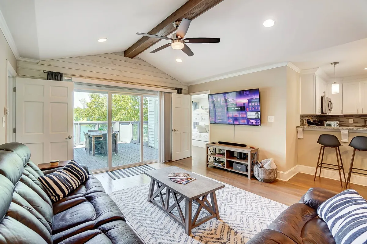 A modern living area featuring a reclining sofa, coffee table, and television, with large sliding glass doors revealing a balcony and abundant natural light. The area feels open, welcoming, and connected to the outdoors—ideal for both work and relaxation.